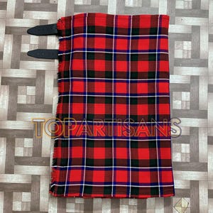 Peut inclure: Un kilt à carreaux rouges, noirs et blancs avec des sangles en cuir noir. Le kilt a un bord effiloché et un motif de carrés répétés. Le texte "TOPARTISANS" est visible sur le kilt.