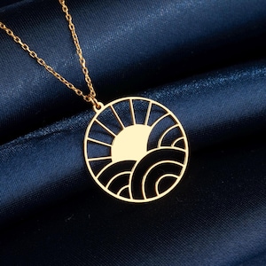 May include: A gold necklace with a circular pendant featuring a sun and waves design. The pendant is cut out, creating a delicate and intricate look.