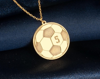 Könnte beinhalten: Goldkette mit einem Fußball-Anhänger. Der Anhänger ist eine runde Scheibe mit einem detaillierten Fußball-Design und der Nummer 5.