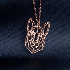 May include: A rose gold necklace featuring a geometric dog pendant. The pendant is a stylised outline of a dog's head, with a minimalist design.