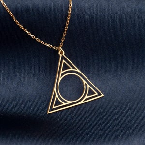 Op de afbeelding: Een gouden ketting met een geometrische driehoekige hanger met een cirkel erin. De hanger heeft een delicaat, ingewikkeld ontwerp.