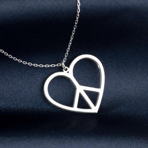 May include: A silver necklace with a heart-shaped pendant featuring a peace sign cutout. The necklace is on a dark blue fabric background.