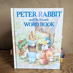 May include: A vintage children's book titled "Peter Rabbit and His Friends Word Book". The cover features a colorful illustration of Peter Rabbit and his friends, including a kitten, a hedgehog, a duck, and a squirrel, all gathered around a tree.