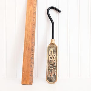 May include: A vintage brass and black metal door hook with the word "OPEN" in embossed letters. The hook is approximately 10 inches long and has a decorative rectangular handle.