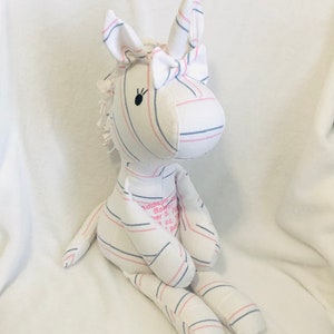 May include: A white and pink striped unicorn stuffed animal with a pink bow. The unicorn has black embroidered eyes and the text "Addison Baby Girl November 5, 2021 7 lb 1 oz 19" is embroidered on the back.