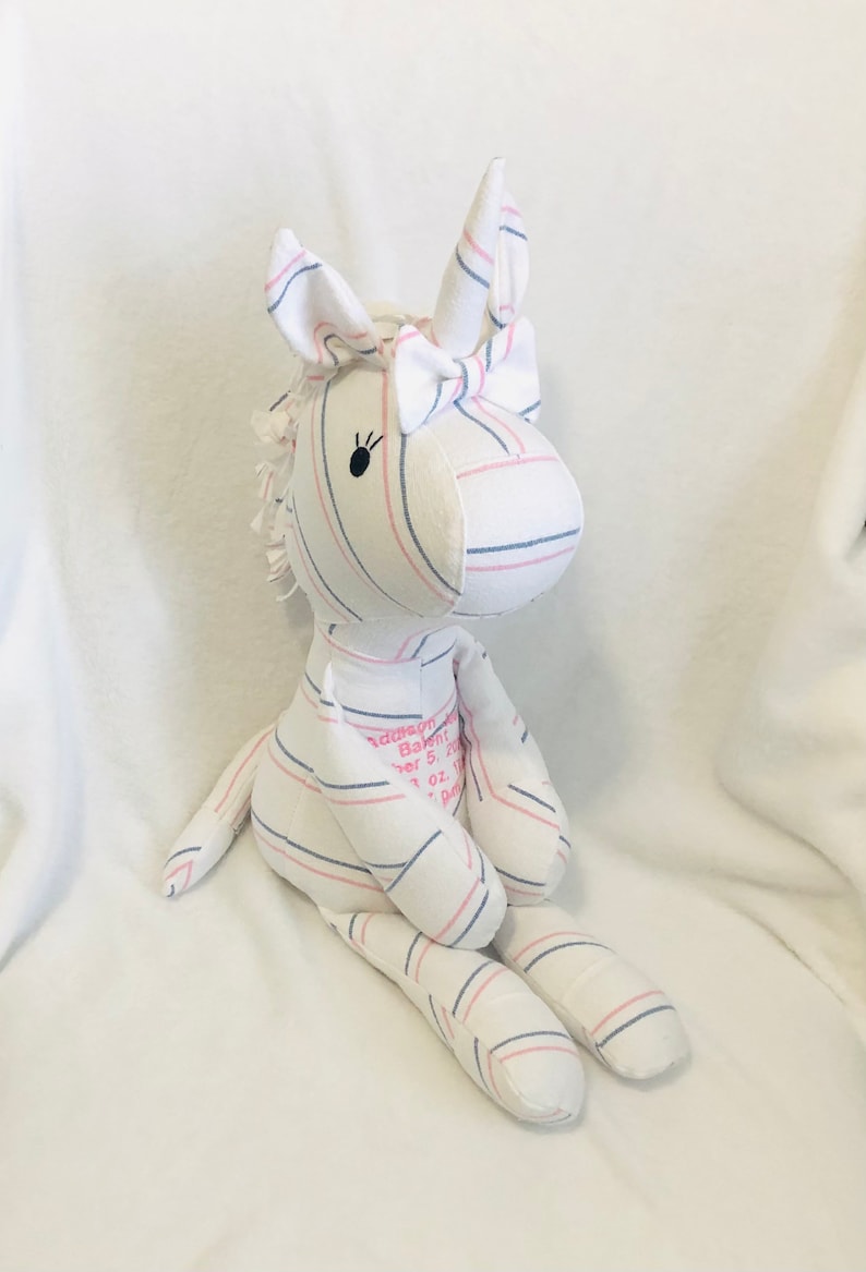 May include: A white and pink striped unicorn stuffed animal with a pink bow. The unicorn has black embroidered eyes and the text "Addison Baby Girl November 5, 2021 7 lb 1 oz 19" is embroidered on the back.
