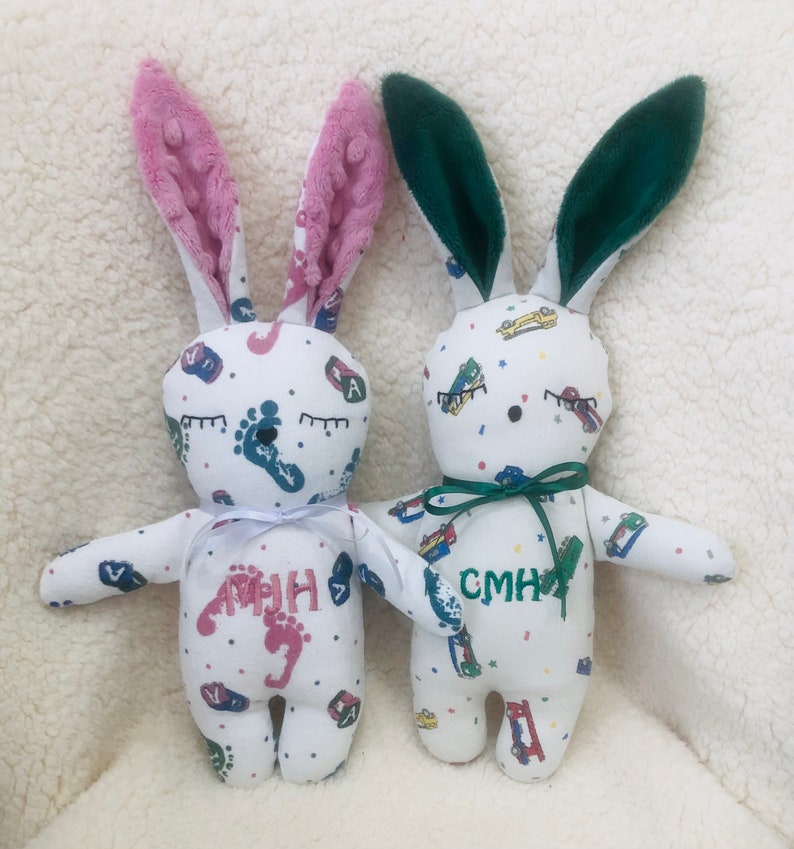 May include: Two white bunny plushes with embroidered eyes and footprints. One bunny has pink ears and the name "AMHH" embroidered on the front. The other bunny has green ears and the name "CMHH" embroidered on the front.