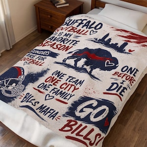 May include: A white fleece blanket featuring blue and red graphics including a football helmet, a buffalo silhouette, and a city skyline. Text reads: Buffalo football is my favorite season, Sundays are for football, One team one city one family, Bills Mafia, One before I die, and Go Bills.