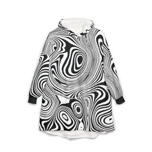 Puede incluir: Una manta con capucha en blanco y negro con un patrón abstracto y arremolinado. El interior de la capucha y el ribete son blancos. La manta tiene mangas largas y un bolsillo de canguro.