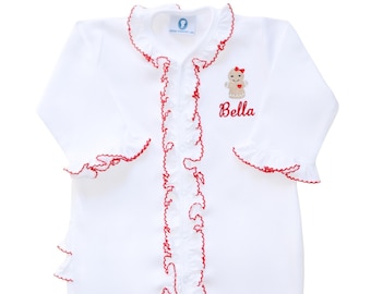 May include: A white long-sleeved footed sleeper featuring a ruffled collar and front placket trimmed in red. The garment includes an embroidered gingerbread person with a red bow and the name Bella stitched in red thread on the upper left chest.