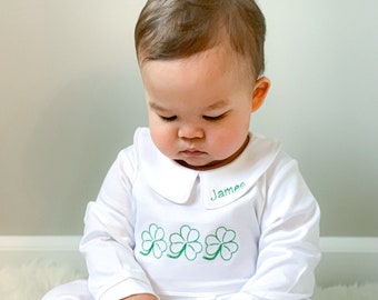 Könnte beinhalten: Ein weißer Baby-Strampler mit einem grünen Kleeblatt-Design und dem Namen "James" auf dem Kragen gestickt.