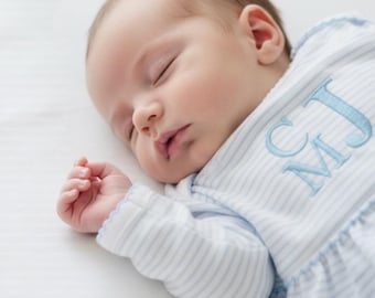 May include: A sleeping infant wearing a long-sleeved, light blue and white striped garment with a scalloped edge at the cuff. The garment features the embroidered letters CJ in a light blue thread on the upper chest area.