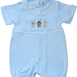 May include: A light blue baby romper with short sleeves and a white collar. Three embroidered dogs wearing party hats are on the front of the romper.