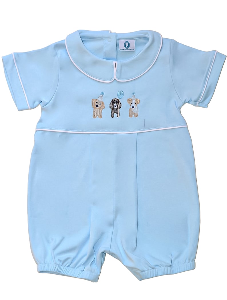 May include: A light blue baby romper with short sleeves and a white collar. Three embroidered dogs wearing party hats are on the front of the romper.