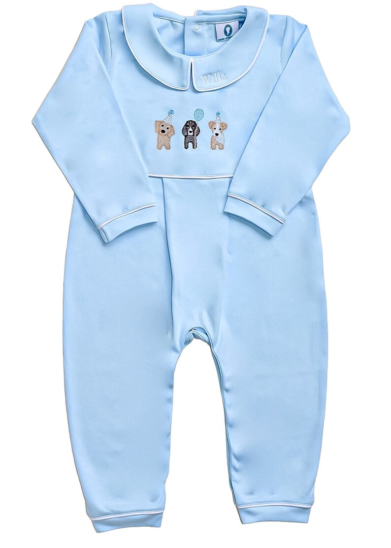 May include: A light blue baby onesie with a white collar and white trim. The onesie has an embroidered design of three dogs wearing party hats. The text "Will" is embroidered on the collar.