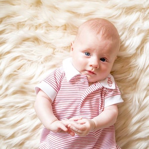 May include: A baby wearing a red and white striped onesie with a white collar and the letters "CDM" embroidered on the collar.