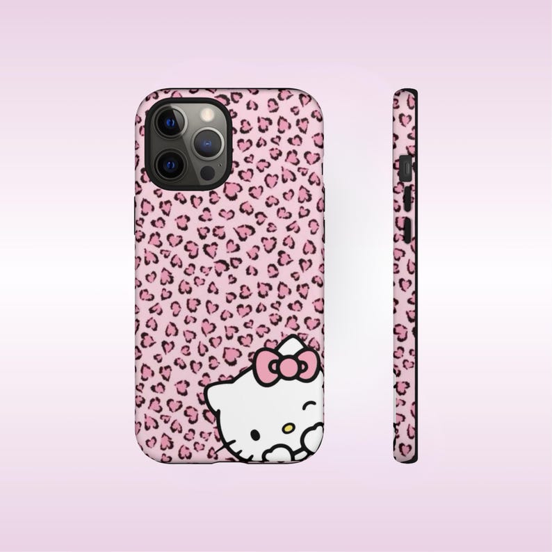 May include: Pink phone case with a leopard print pattern of black hearts. The case features a white Hello Kitty graphic with a pink bow. The side view of the case shows the buttons and camera details.