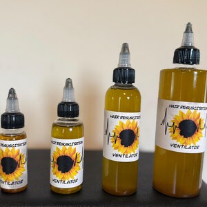 Könnte beinhalten: Vier transparente Flaschen Haaröl mit schwarzen Kappen und Applikatorspitzen. Jede Flasche hat ein weißes Etikett mit einem Sonnenblumenmuster und den Worten "Hair Resuscitation" und "Ventilator". Das Öl hat eine goldgelbe Farbe.