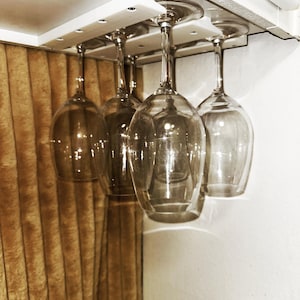 Può includere: Un porta bicchieri da vino bianco sottopensile con quattro bicchieri da vino appesi. Il supporto è fissato a un soffitto bianco.