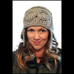 May include: A gray crocheted hat with ear flaps. The hat has a unique design with a braided pattern on the top.