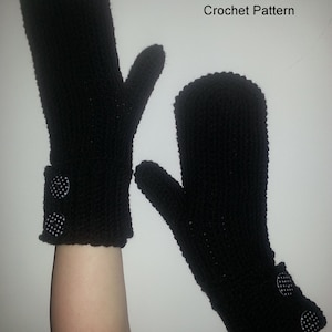May include: A pair of black crocheted mittens with white button accents. The mittens are shown against a white background.  The text "CRABMITTENS Crochet Pattern" is at the top of the image.