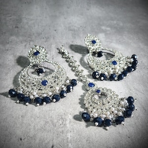 May include: An elaborate silver-coloured earring and headpiece set. The earrings and headpiece have a circular design, with embedded blue gemstones and navy blue beads. Small white beads are also incorporated into the design.
