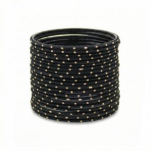 May include: A collection of black bangles adorned with tiny gold-coloured spots. The bangles are circular and seem to be made from a solid material. The gold spots are uniformly distributed across the surface of the bangles.