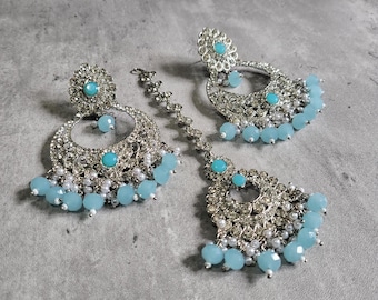 May include: A set of silver earrings and a matching maang tikka with blue and white beads. The earrings are large and circular with intricate designs. The maang tikka is a traditional Indian headpiece.