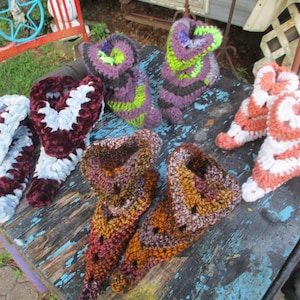 May include: Four pairs of handmade crochet slippers in various color combinations including maroon and light blue, purple and lime green, brown and bronze, and coral and white. Each pair features a textured yarn construction with a high-top design.