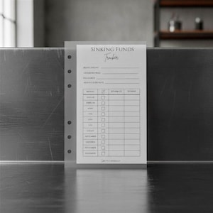 May include: A translucent, punched planner insert titled Sinking Funds Tracker with black printed text. The form includes fields for description, total amount, due date, and monthly rate, followed by a table listing months from January to December.