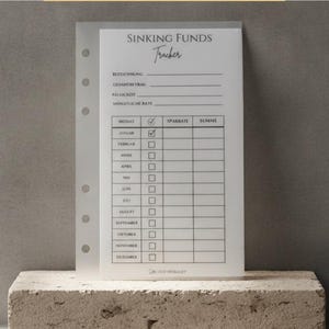 Ein hochkant gestaltetes, transparentes Einlegeblatt für einen Planer mit Ringbindung, beschriftet als „Sinking Funds Tracker“. Das Formular ist auf Deutsch verfasst und dient zum Sparen für bestimmte Ziele. Es enthält Felder für Bezeichnung, Gesamtbetrag, Fälligkeit und monatliche Rate sowie eine Tabelle mit den zwölf Monaten (Januar bis Dezember), Kontrollkästchen, einer Spalte für die Sparrate und einer Spalte für die Summe.