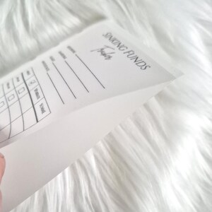 May include: A white paper sinking funds tracker sheet with black printed text and lines. The document features the header SINKING FUNDS Tracker, followed by columns for date, description, and amount, with checkboxes for tracking financial progress.