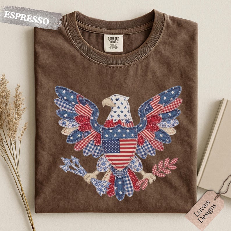 May include: An espresso brown t-shirt featuring a central graphic of a bald eagle composed of various red, white, and blue patterned fabric patches, including stars and stripes. The eagle holds arrows and an olive branch in its talons.