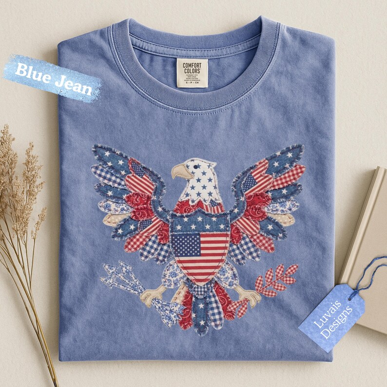 May include: A blue jean colored t-shirt featuring a large eagle graphic composed of various red, white, and blue patterned fabric patches. The eagle holds arrows and a branch, with a central shield displaying the American flag. The label reads Comfort Colors.