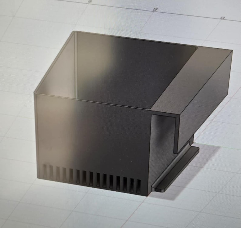 May include: A black, angular, rectangular object with a sloped top and a series of vertical slots along the bottom edge. The design appears to be a 3D rendering or a technical drawing.