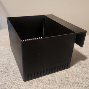 May include: A black rectangular aquarium filter box with a slotted side and a lip for hanging. The box has a series of vertical slots on one side and small horizontal slots on the top edge.