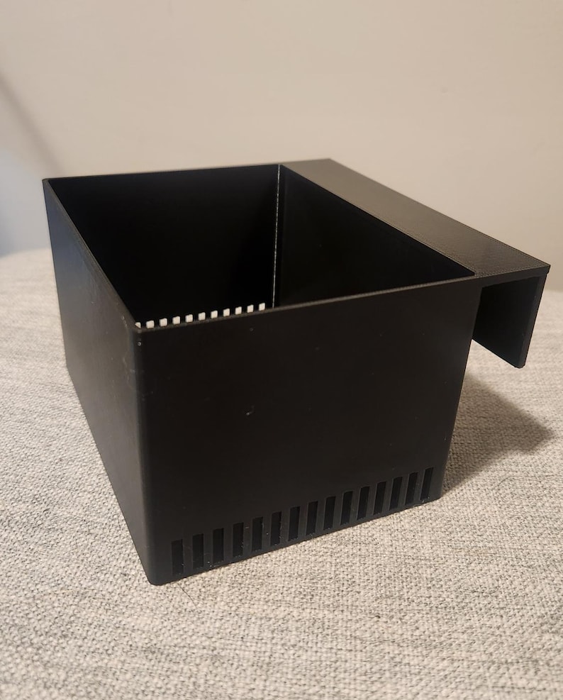 May include: A black rectangular aquarium filter box with a slotted side and a lip for hanging. The box has a series of vertical slots on one side and small horizontal slots on the top edge.