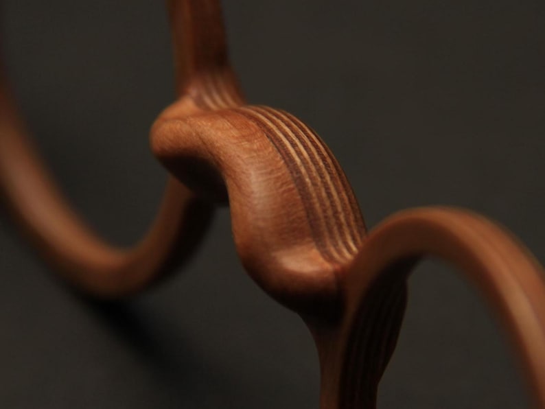 May include: A smooth, reddish-brown wooden object featuring a series of interconnected, curved, and circular shapes. The wood grain is clearly visible, showcasing layered textures and a polished finish that highlights the natural curves of the form.