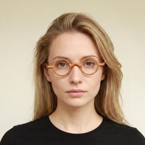 May include: Round eyeglasses with a light brown wooden frame and a high bridge. The circular lenses are clear and set within a smooth, polished wood rim that connects directly to the temples, creating a cohesive and natural look for the eyewear.