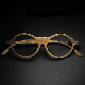 May include: Wooden-framed eyeglasses with round lenses. The glasses are a light brown color and appear to be made of wood. The arms of the glasses are also wooden and have a slight curve. The background is black.