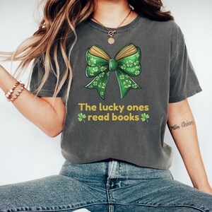 May include: A dark gray t-shirt with a green and yellow book bow and the text "The lucky ones read books" with shamrock symbols.