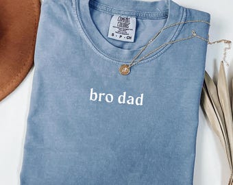 Puede incluir: Una camiseta azul claro con el texto "bro dad" en letras blancas.