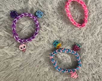 Flerfärgat set med tre gummibandsarmband, ljusrosa, rosa och blå, ljuslila och mörklila gummibandsarmband.