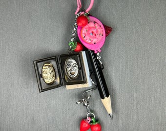 Könnte beinhalten: Eine rosa und silberne Charm-Kette mit verschiedenen Charms, darunter ein Mini-Buch, ein Bleistift, ein Donut und Erdbeeren.