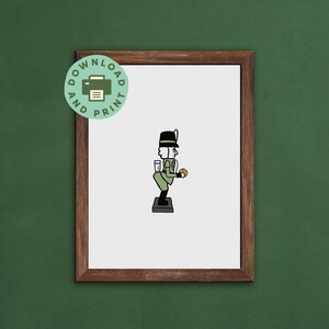 Op de afbeelding: Een ingelijste print met een cartoon illustratie van een notenkraker soldaat. De soldaat is in groen en zwart, met een drankje en een koekje. De print heeft een witte achtergrond en een bruine lijst. Een groene en witte cirkel zegt "Downloaden en afdrukken".