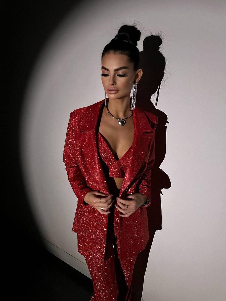May include: A red sparkly blazer and pants set. The blazer has a notched lapel and a single button closure. The pants have a straight leg.