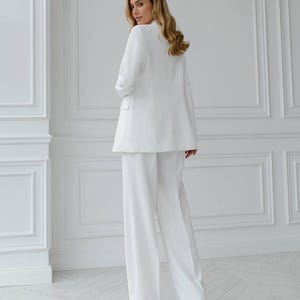 May include: A white suit consisting of a blazer and wide-leg pants. The blazer has a classic design with lapels and pockets. The pants are long and flowing, creating a sleek, elegant silhouette. The suit is made of a smooth, solid white fabric.