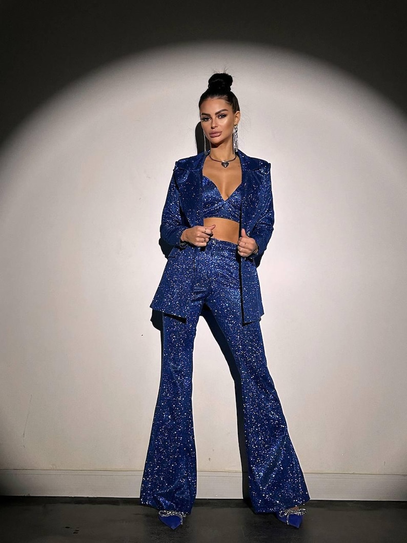 May include: A woman wearing a blue sparkly blazer and matching pants. The blazer has a notched lapel and the pants are flared.