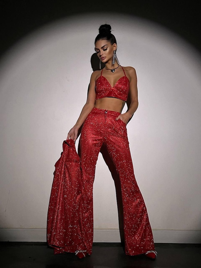 May include: A red sequined crop top and matching wide-leg pants. The top has a halter neckline and a heart-shaped cutout. The pants have a high waist and a wide leg.