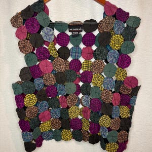 May include: A colorful, patchwork vest made of fabric circles in various patterns and colors, including purple, green, yellow, and brown. The vest is hanging on a wooden hanger. The brand name "NOTATIONS" is visible on the label.